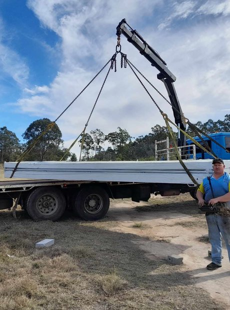 A man stands in front of a crane truck, lifting up a large stack of metal.