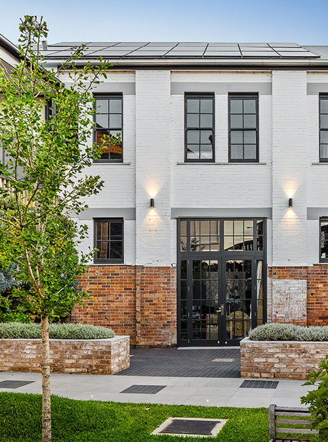 An old brick building that has been modernised and is painted white halfway up. There are trees and a lawn in front of the front door