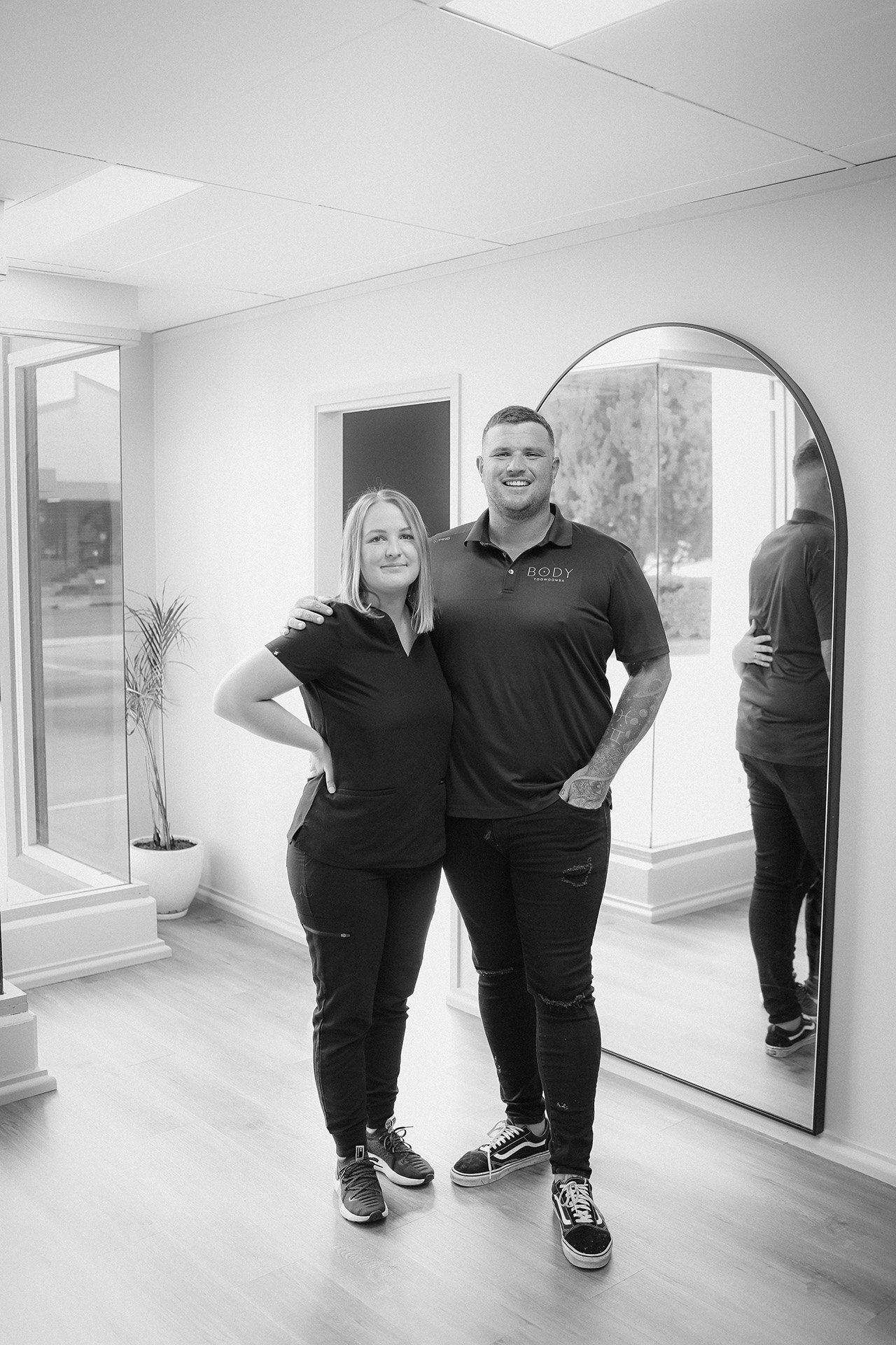 Melinda and Jason stand together in their studio. A large mirror is behind them.